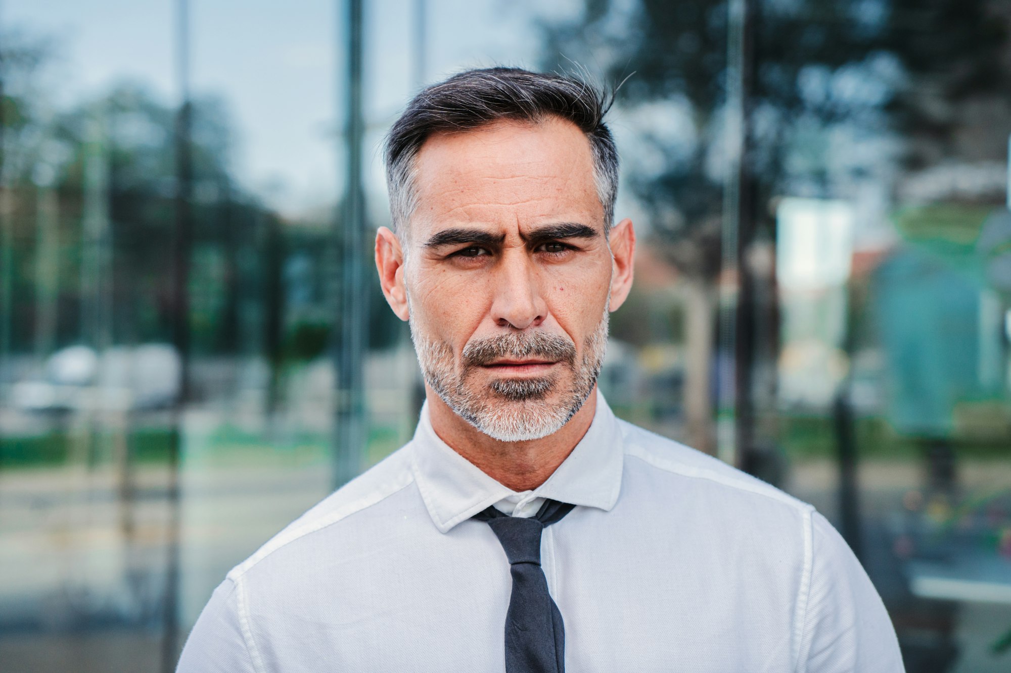 Individual close up portrait of serious mature businessman looking pensive at camera at workplace