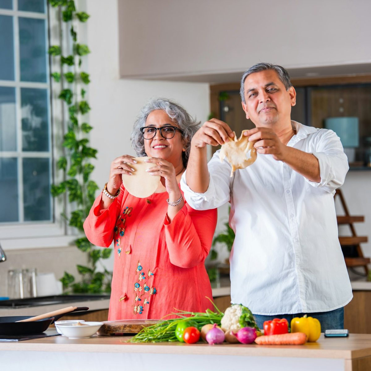 Indian asian senior woman teaches husband how to cook, to make a round chapati or roti